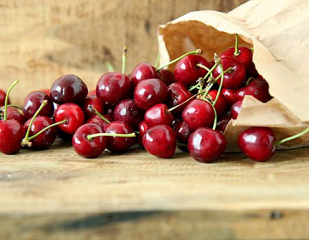 A paper bag spills fresh, red cherries onto a wooden surface, creating a rustic and appetizing scene.